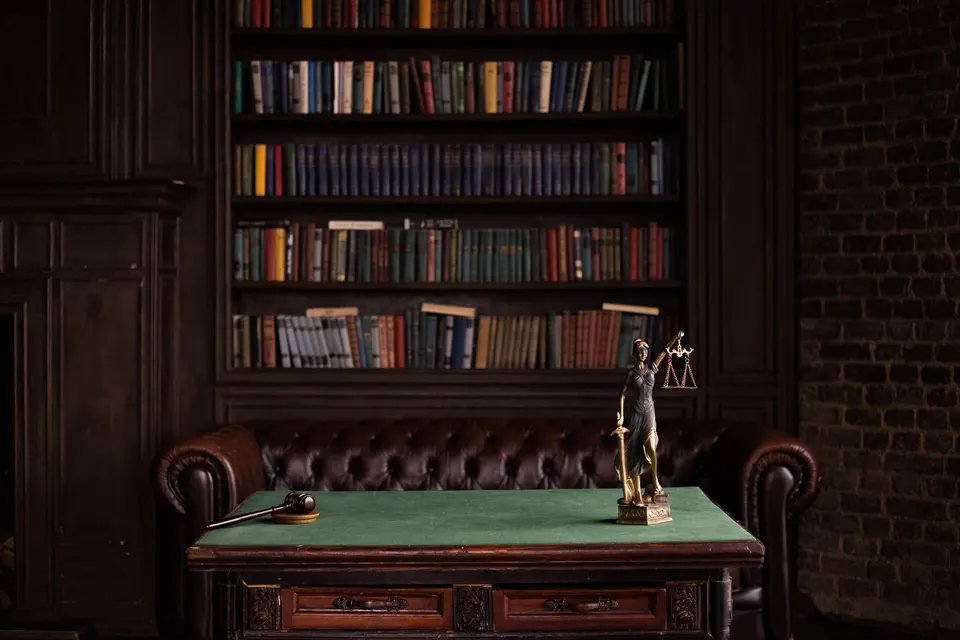 A study lined with bookshelves, with a leather chair and a figure of Lady Justice on a green table.