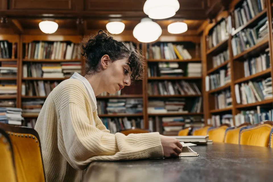 A student reading at a long table in a wood-paneled library.